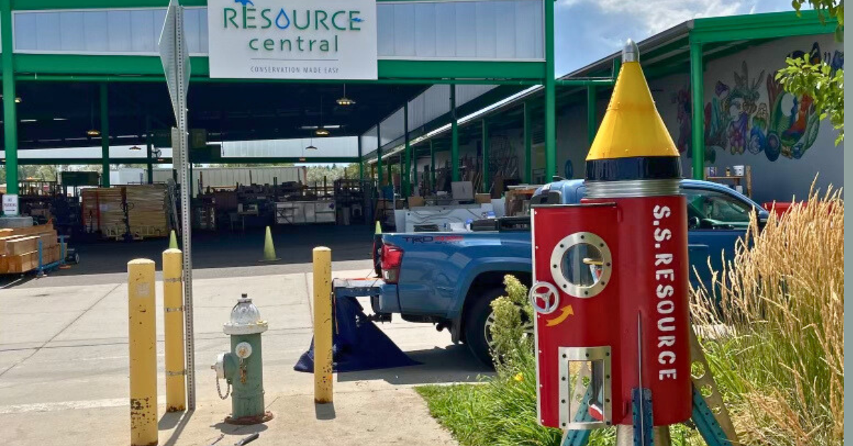 A colorful rocket in front of a blue truck and the Resource Central facility.