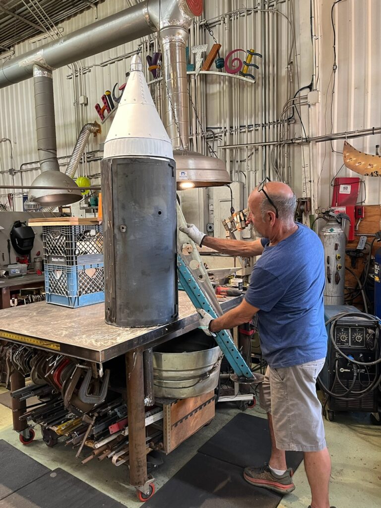 An artist assembles a metal structure in a workshop. 