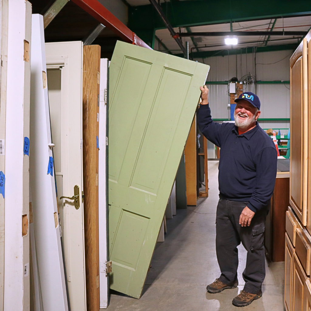 A volunteer smiles while organizing doors in a warehouse.