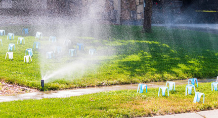 A Resource Central team member conducting a Slow the Flow sprinkler evaluation, holding a tablet and standing near a running sprinkler head.