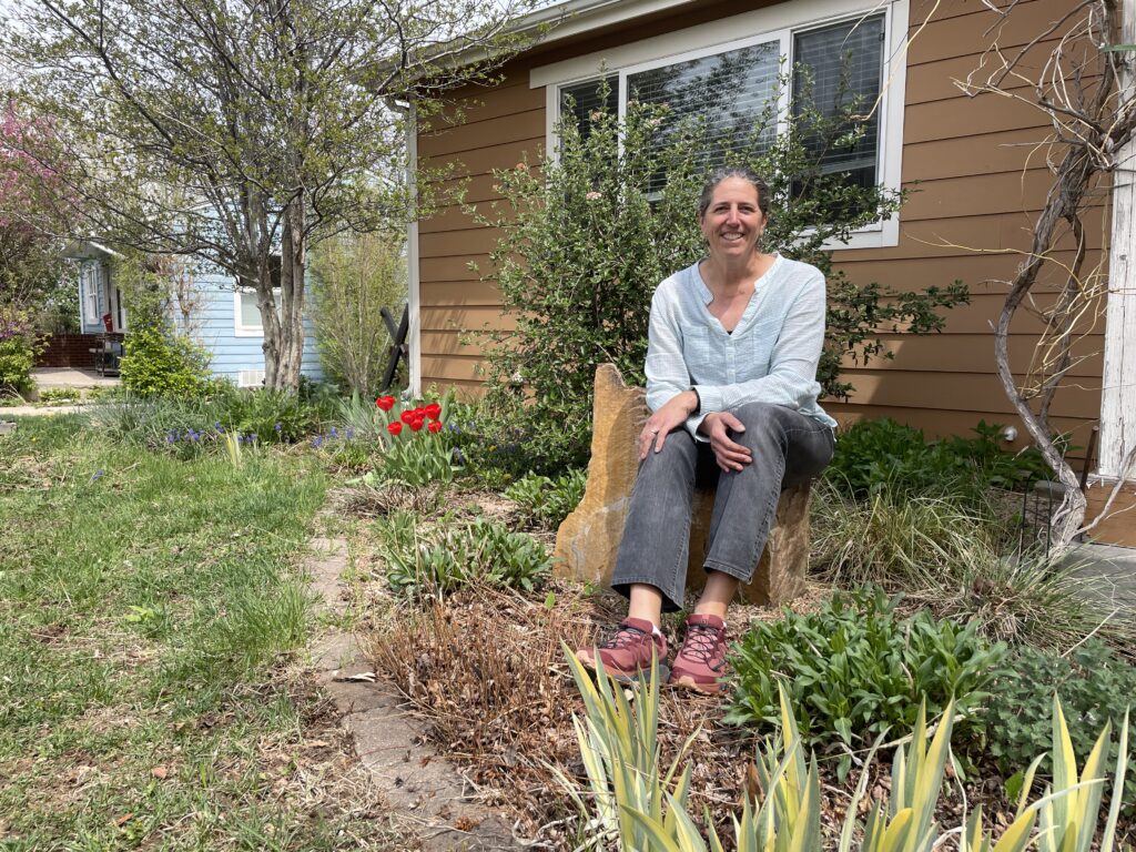 A woman (Kerry White) sitting on a rock in her front yard garden.