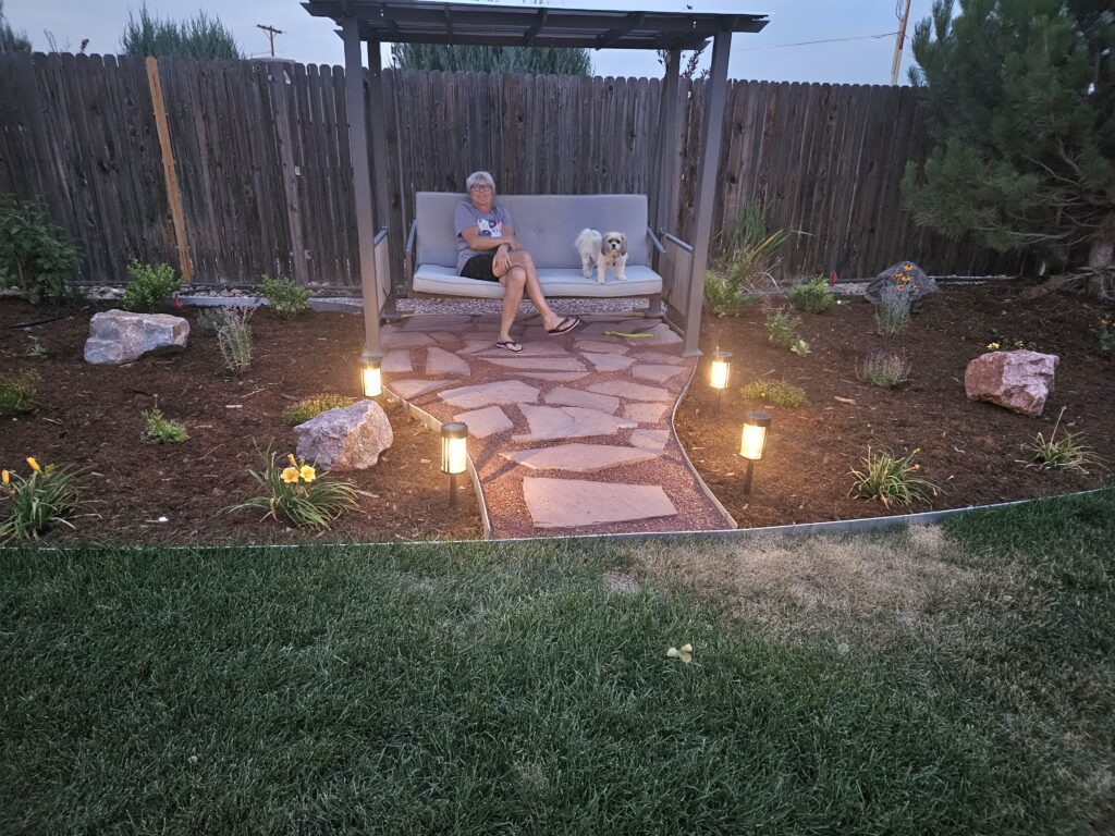 person sitting on an outdoor swing with their dog in a new garden area of a backyard.