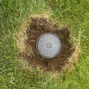 sprinkler head from above with hole dug around it in the lawn.