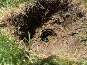 A deep hole dug in a lawn with a sprinkler line on the inside.