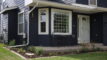 The front yard of a home, with some grass and a garden planted around the patio.