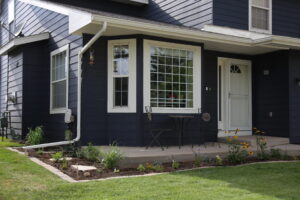 The front yard of a home, with some grass and a garden planted around the patio.