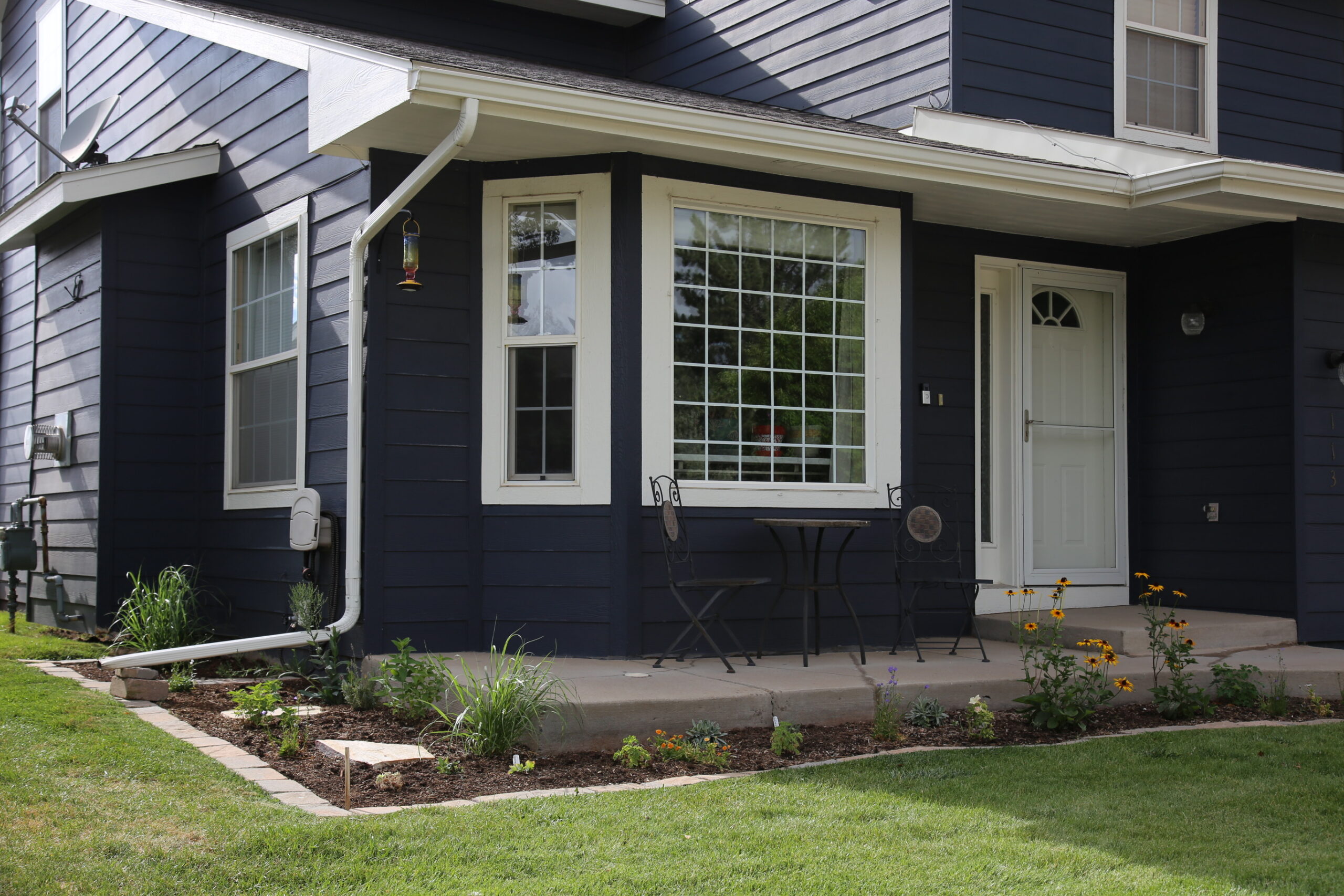 The front yard of a home, with some grass and a garden planted around the patio.